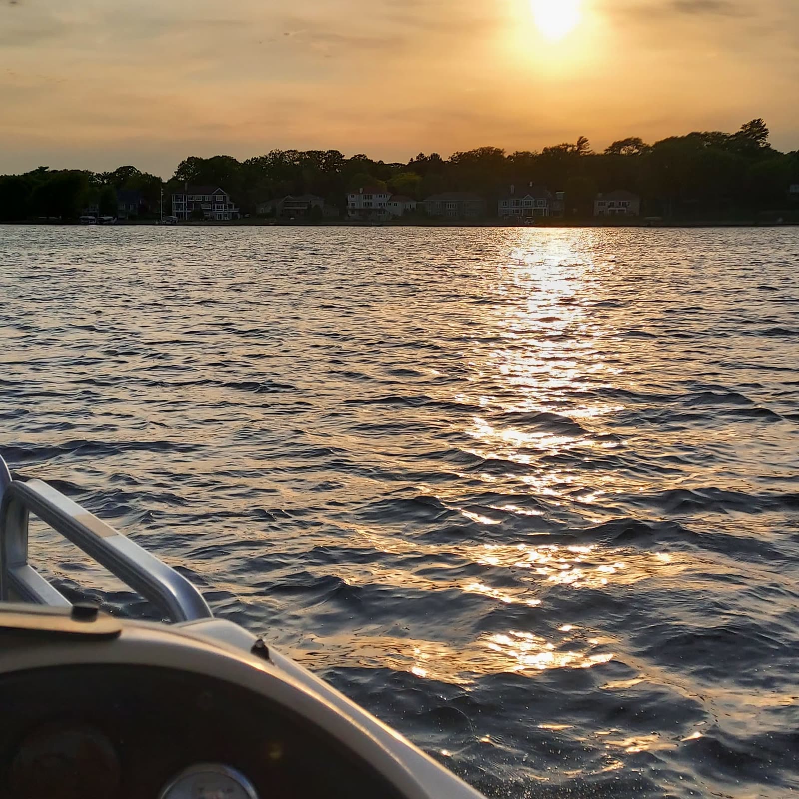 Golden sunset over a lake, sun laying a bright path on the water, shot over the bow of a boat