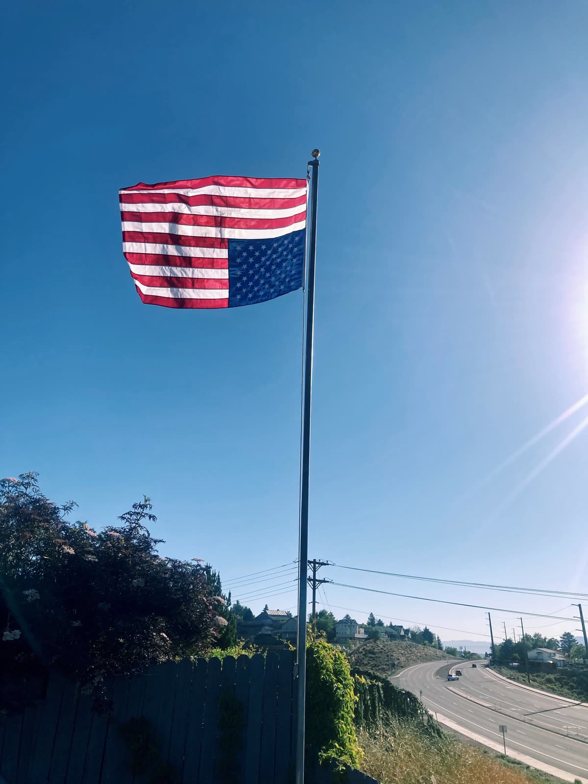 A United States flag flown upside down on a pole against a clear blue sky above a road
