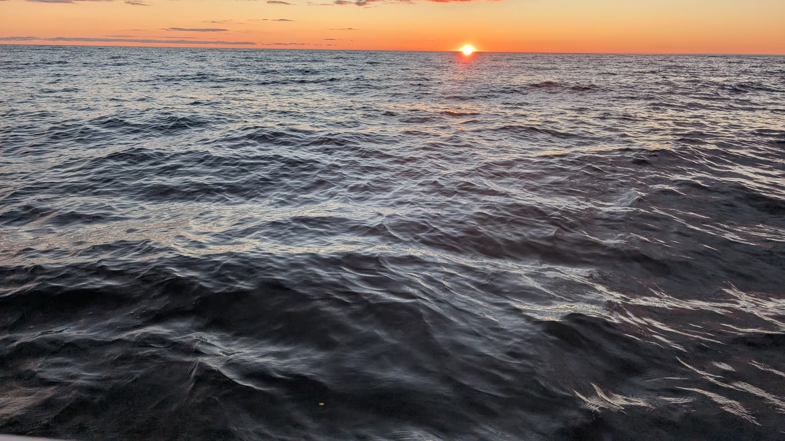 Choppy lake water at sunset, orange band on the horizon, sun just above the water