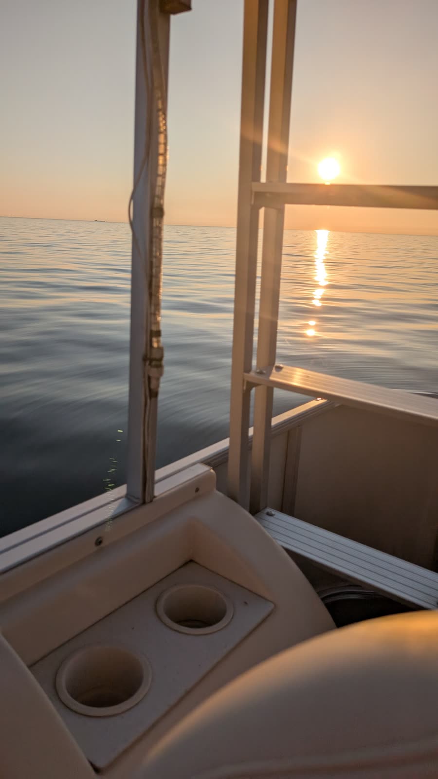 Sunset seen through the frame of a pontoon boat, cupholders in the foreground