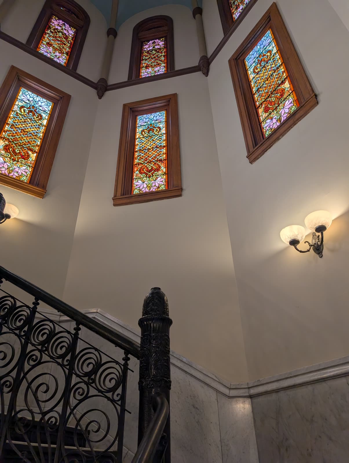 Looking up at a tower of Celtic-knot stained-glass windows over marble and an iron rail